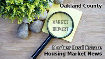 Tabletop has rocks and plant next to a yellow piece of paper with the words market report spelled out beneath a magnifying glass, and more words on the table spell out Oakland County Norber Real Estate Group Housing Market News.